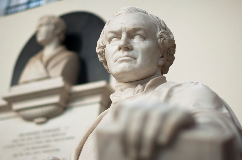 Statue of a man with a resolute expression in a museum setting; a blurred statue is in the background