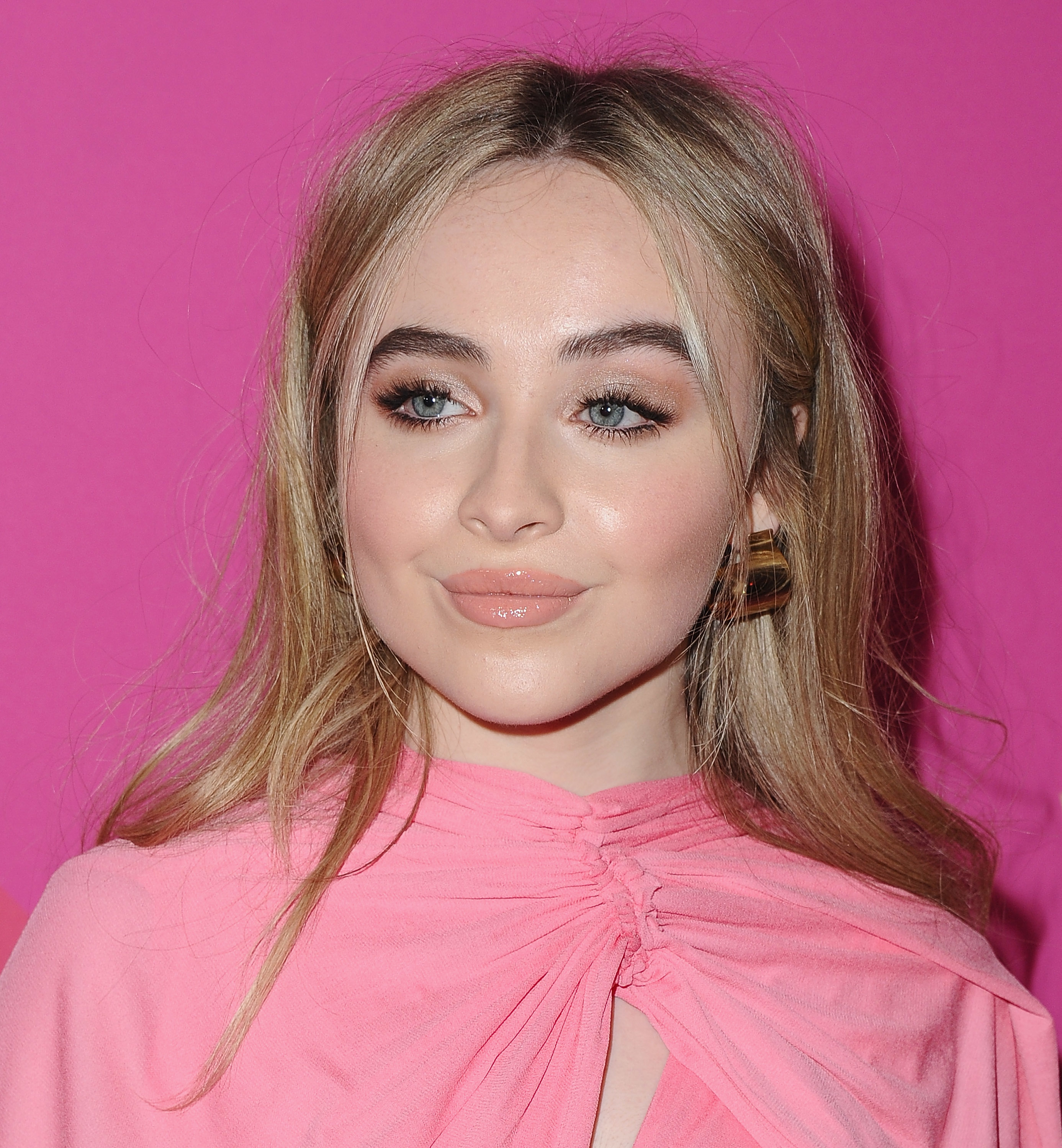 Sabrina Carpenter wearing an outfit with a knotted detail at the neck, and large hoop earrings