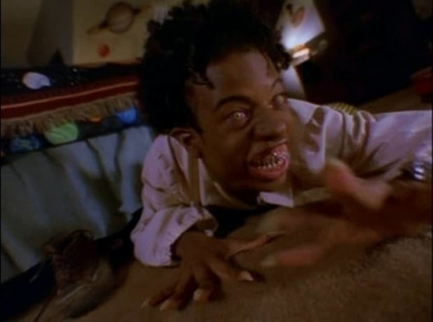 A person with exaggerated features, appearing panicked, crawls on the floor in a dimly lit room