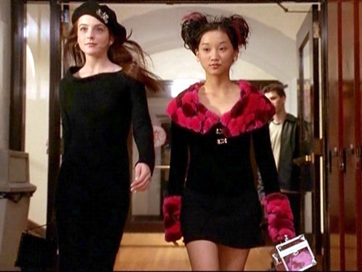 Lindsay Lohan and Brenda Song walk confidently in a hallway, wearing stylish black outfits with red accents