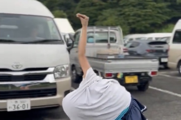 駐車場で白いシャツを使ってポーズをとる人。