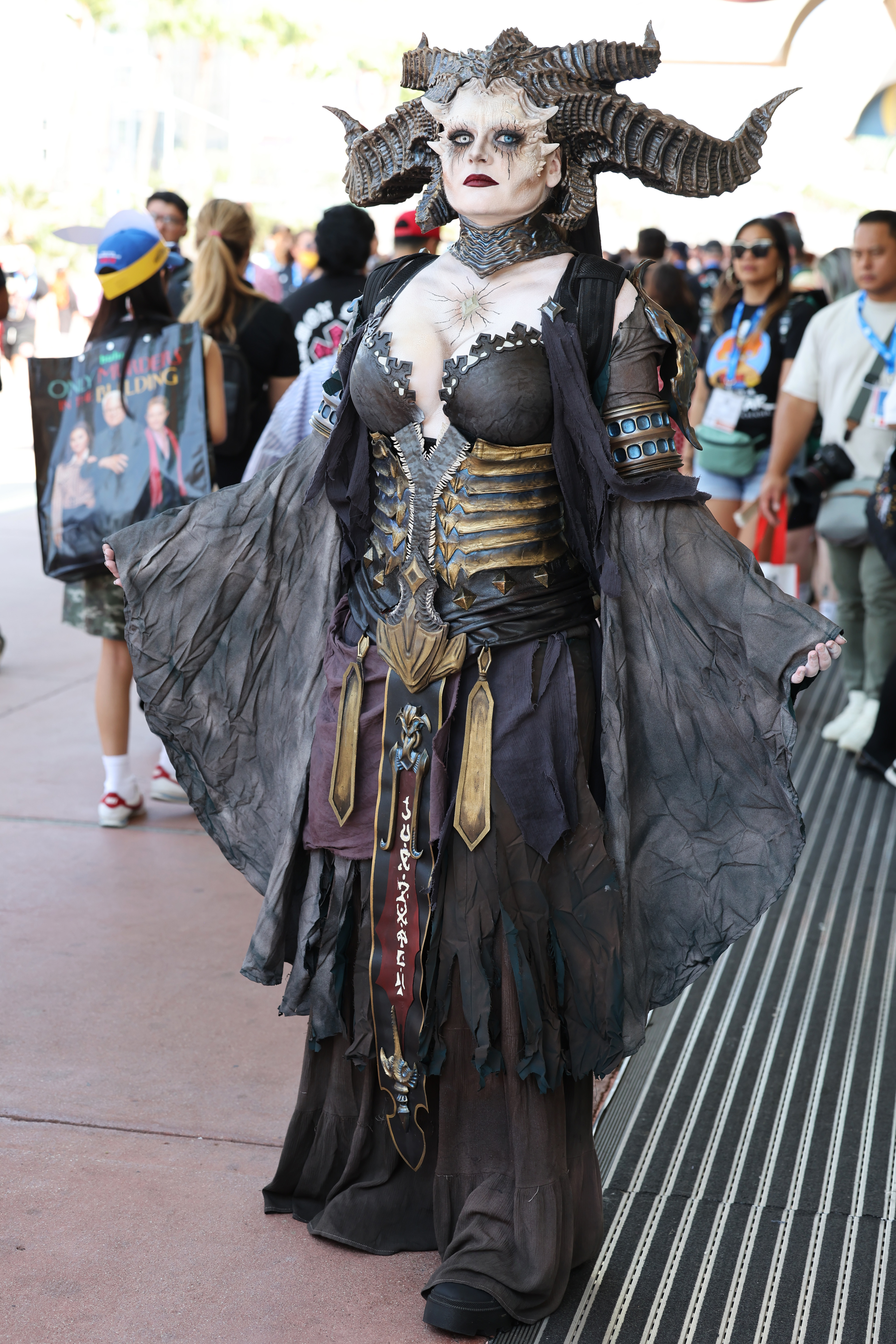 Person in an elaborate, gothic medieval costume with horned headdress and dark, flowing robes standing on a convention floor