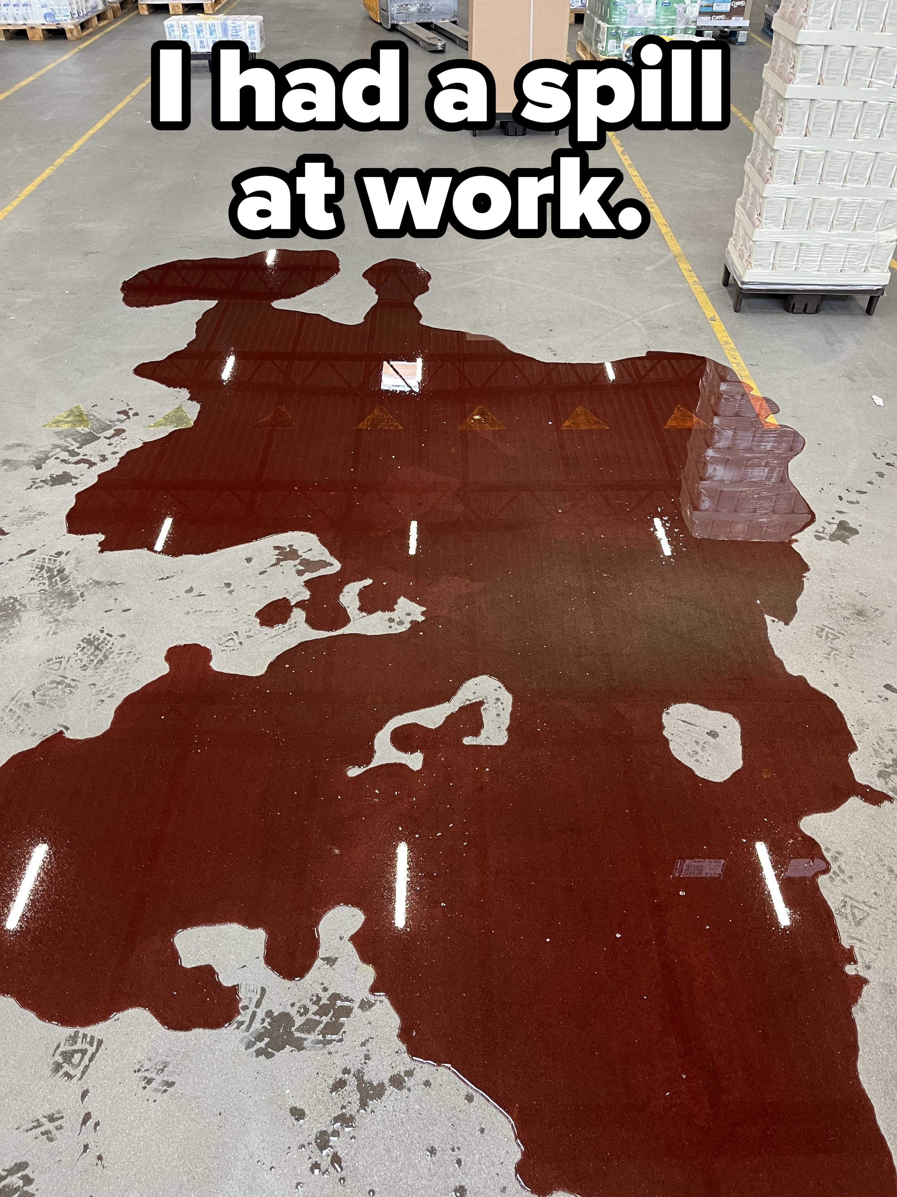A large spill of red liquid on a warehouse floor surrounded by pallets and boxes