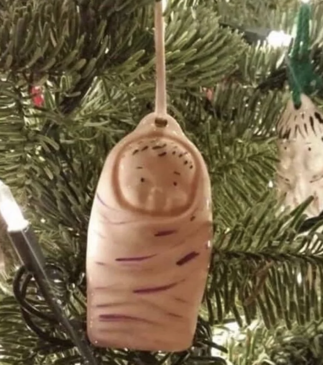 Close-up of a Christmas ornament on a tree branch, shaped like a wrapped baby with simple facial features