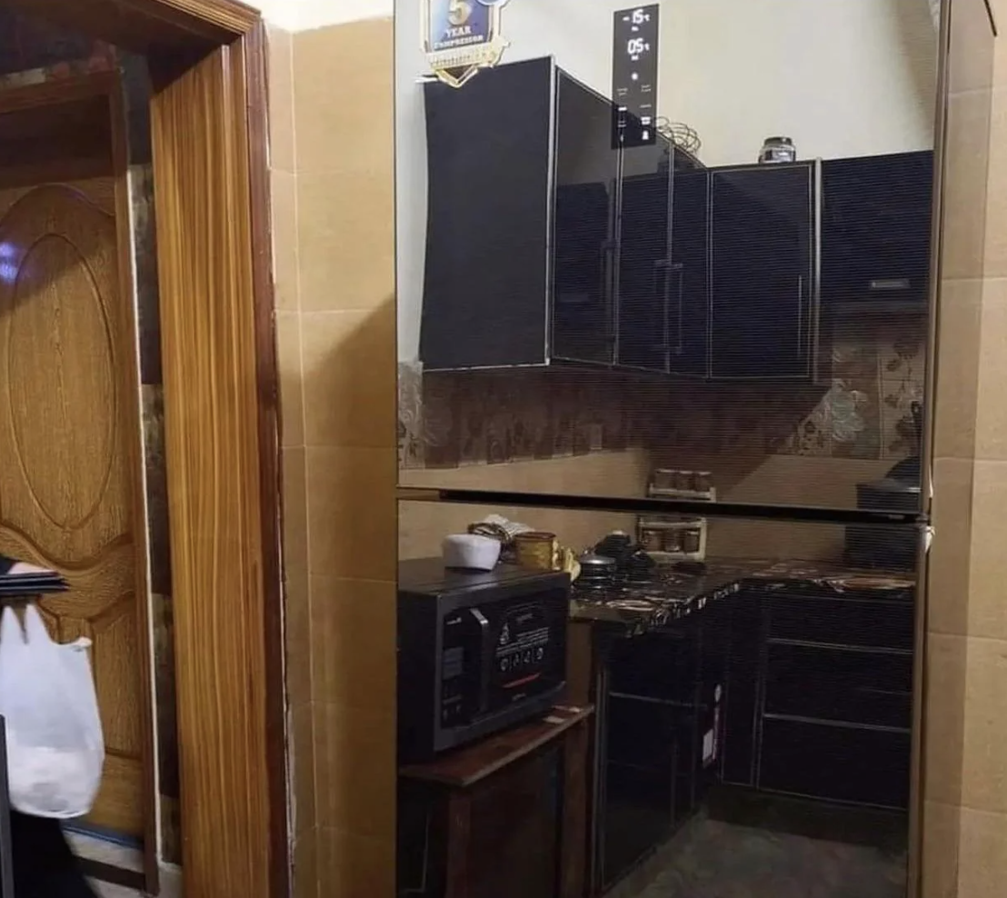 A small, modern kitchen with black cabinets, a microwave, and various kitchen gadgets on the countertops. A door is partially visible on the left side