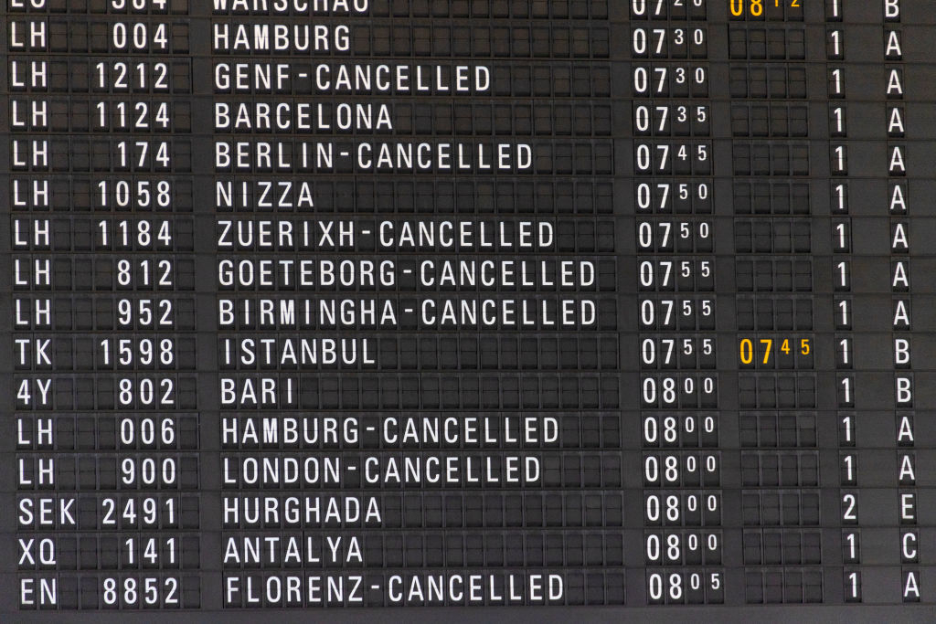 An airport departures board displaying multiple flights to various destinations, with many marked as cancelled