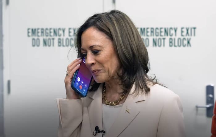 Kamala Harris smiling and holding a phone to her ear, standing in front of an emergency exit
