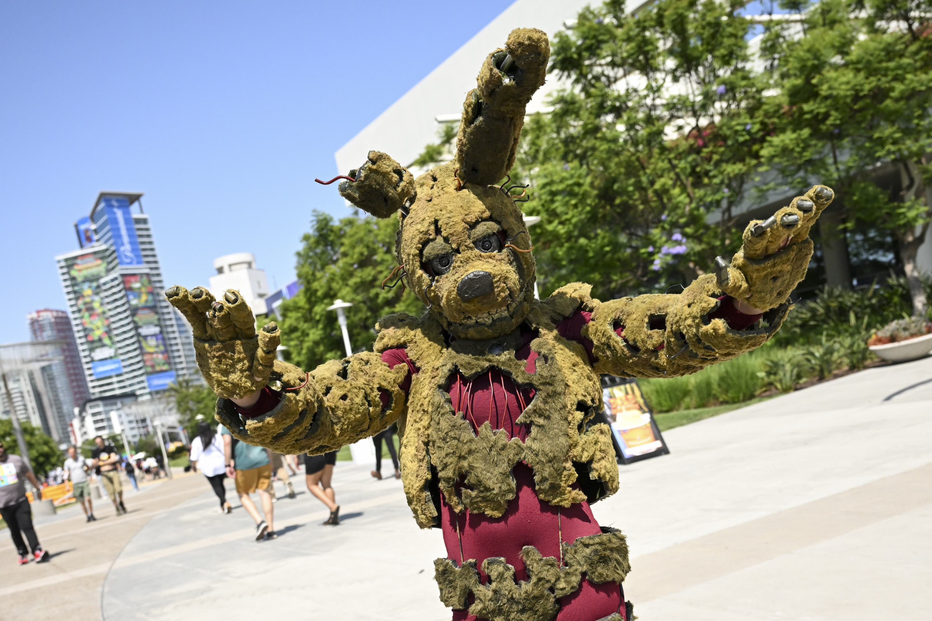 Person dressed in a detailed, tattered rabbit costume with a robotic-like appearance at an outdoor event, with buildings and trees in the background