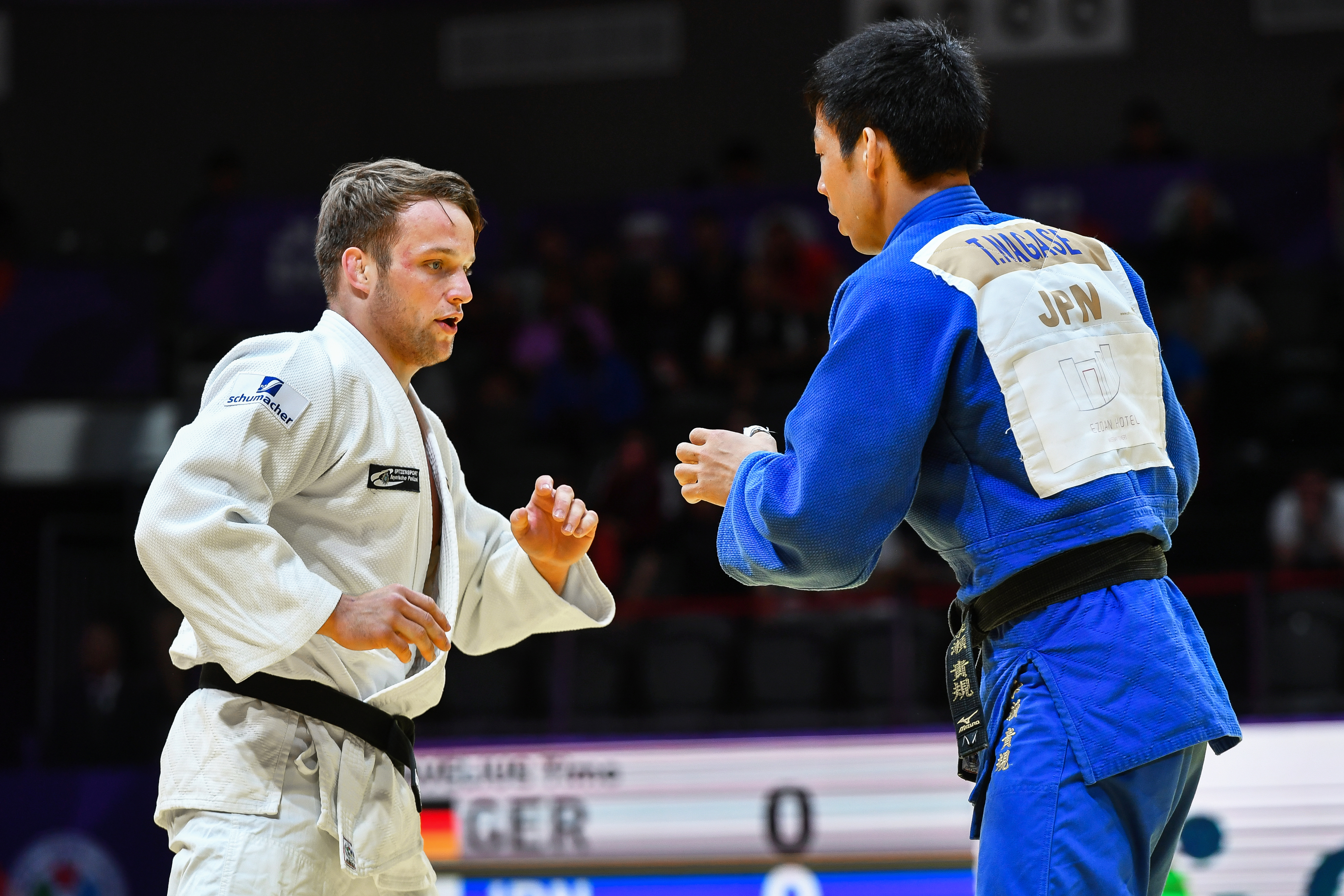 Judo athletes Tim Gramkow (GER) and Takanori Nagase (JPN) face off during a match. Tim Gramkow wears a white gi while Takanori Nagase wears a blue gi