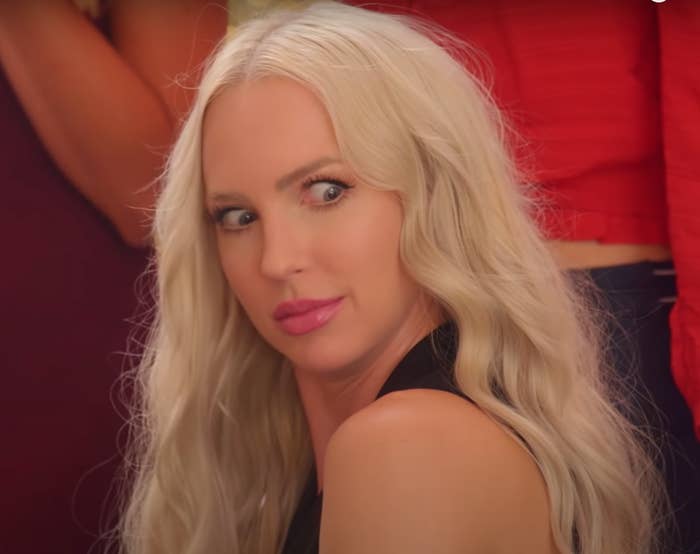 Christine Quinn from Netflix's "Selling Sunset" stares wide-eyed at the camera with other cast members partially visible in the background