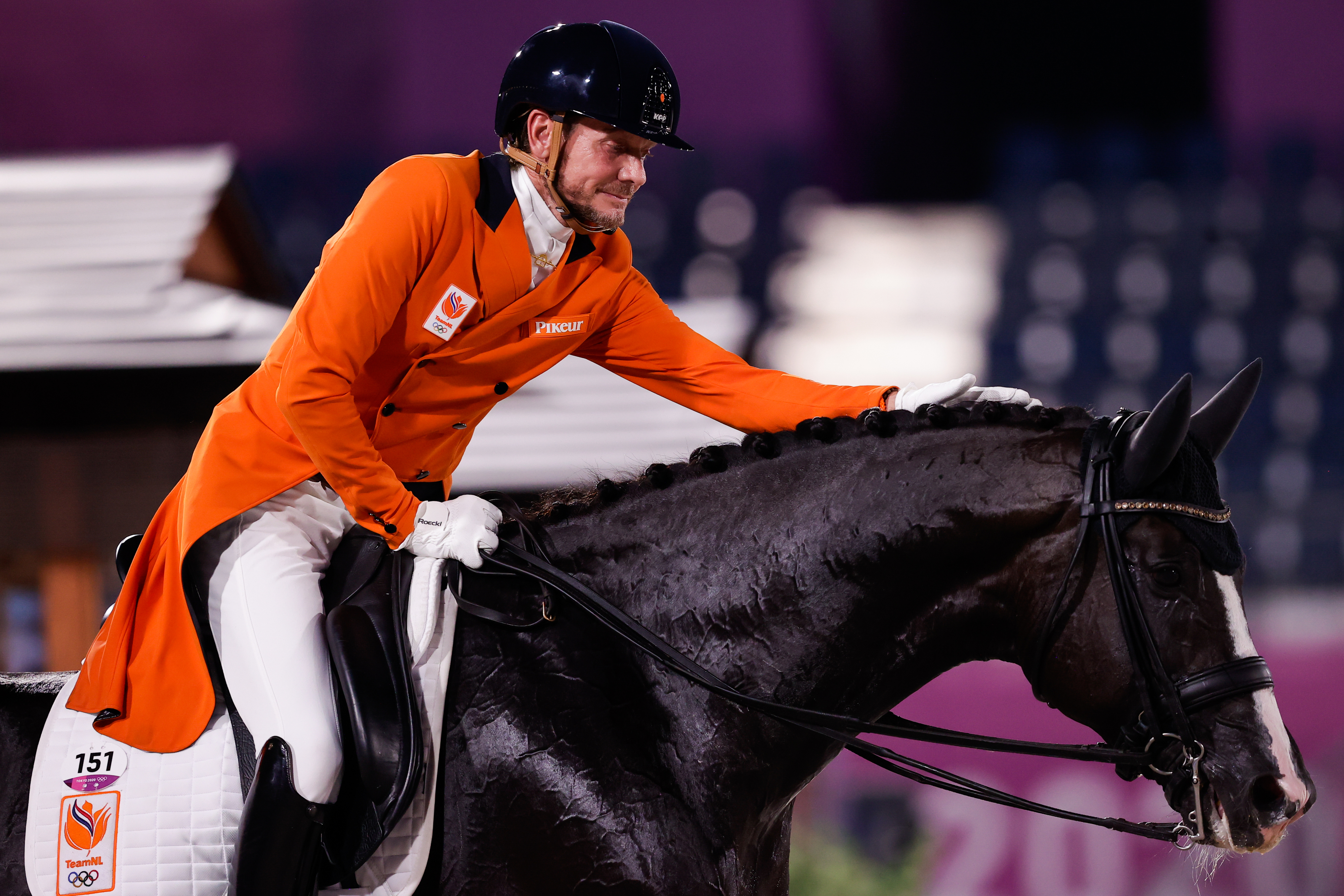 Hans Peter Minderhoud, wearing an orange jacket, white pants, and a helmet, competes in equestrian dressage with his horse at the Olympics
