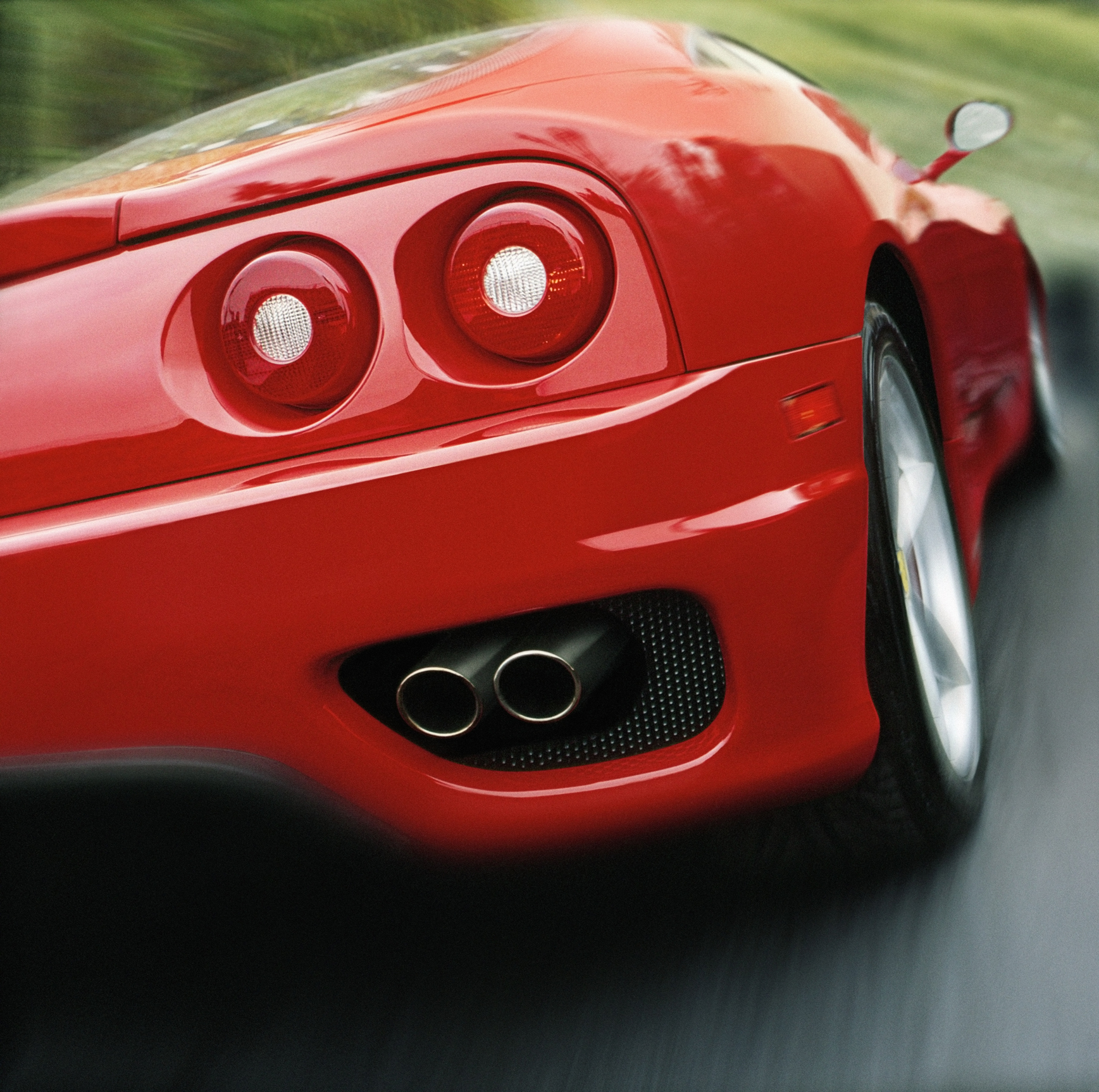 Close-up of the rear of a sports car speeding on a road, featuring its taillights and dual exhaust pipes