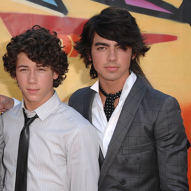 Nick and Joe Jonas are dressed in stylish outfits with collared shirts and ties, posing together in front of a graffiti-style background