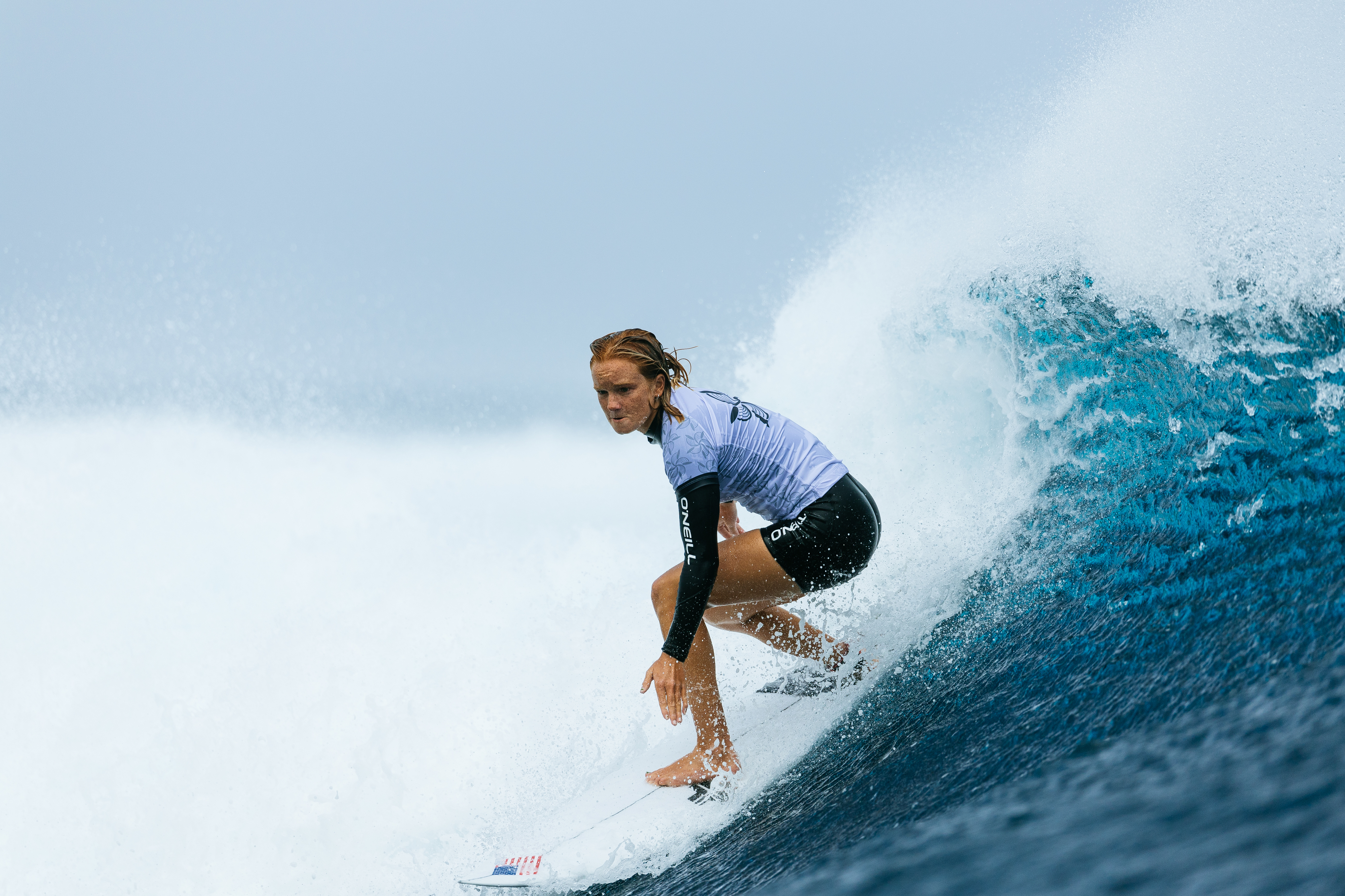 A person wearing a wetsuit rides a large ocean wave on a surfboard, focused and poised