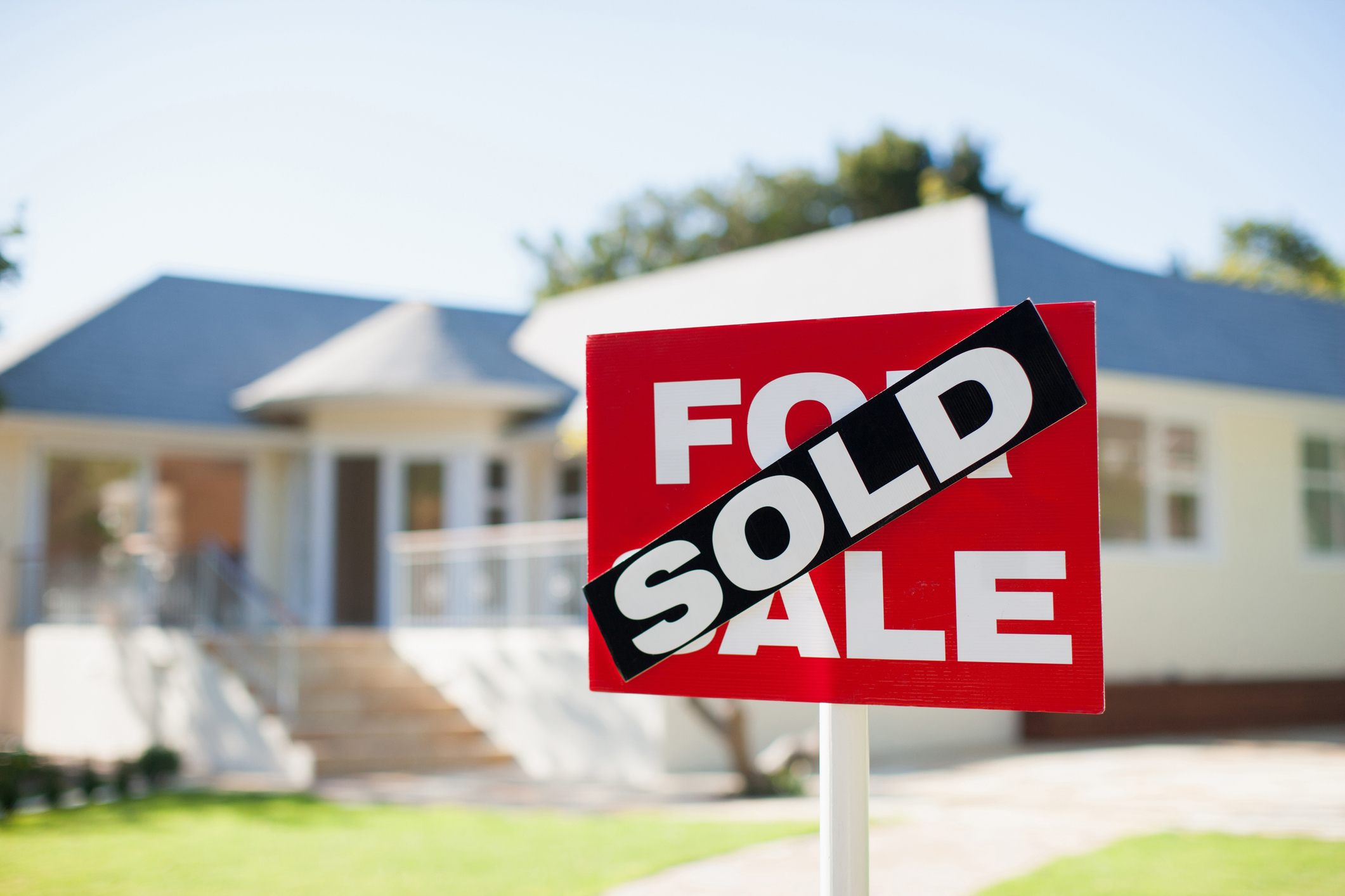 A &quot;For Sale&quot; sign in front of a house with a &quot;Sold&quot; banner across it, indicating the house has been purchased