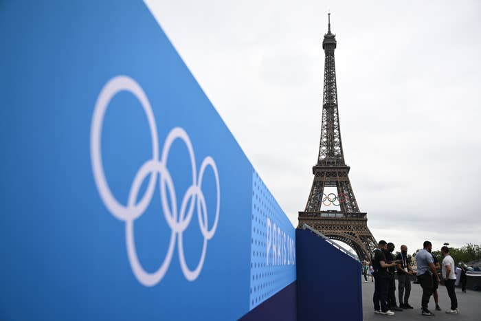 People gather near the Eiffel Tower in Paris, featuring the Olympic rings in preparation for the upcoming Olympics