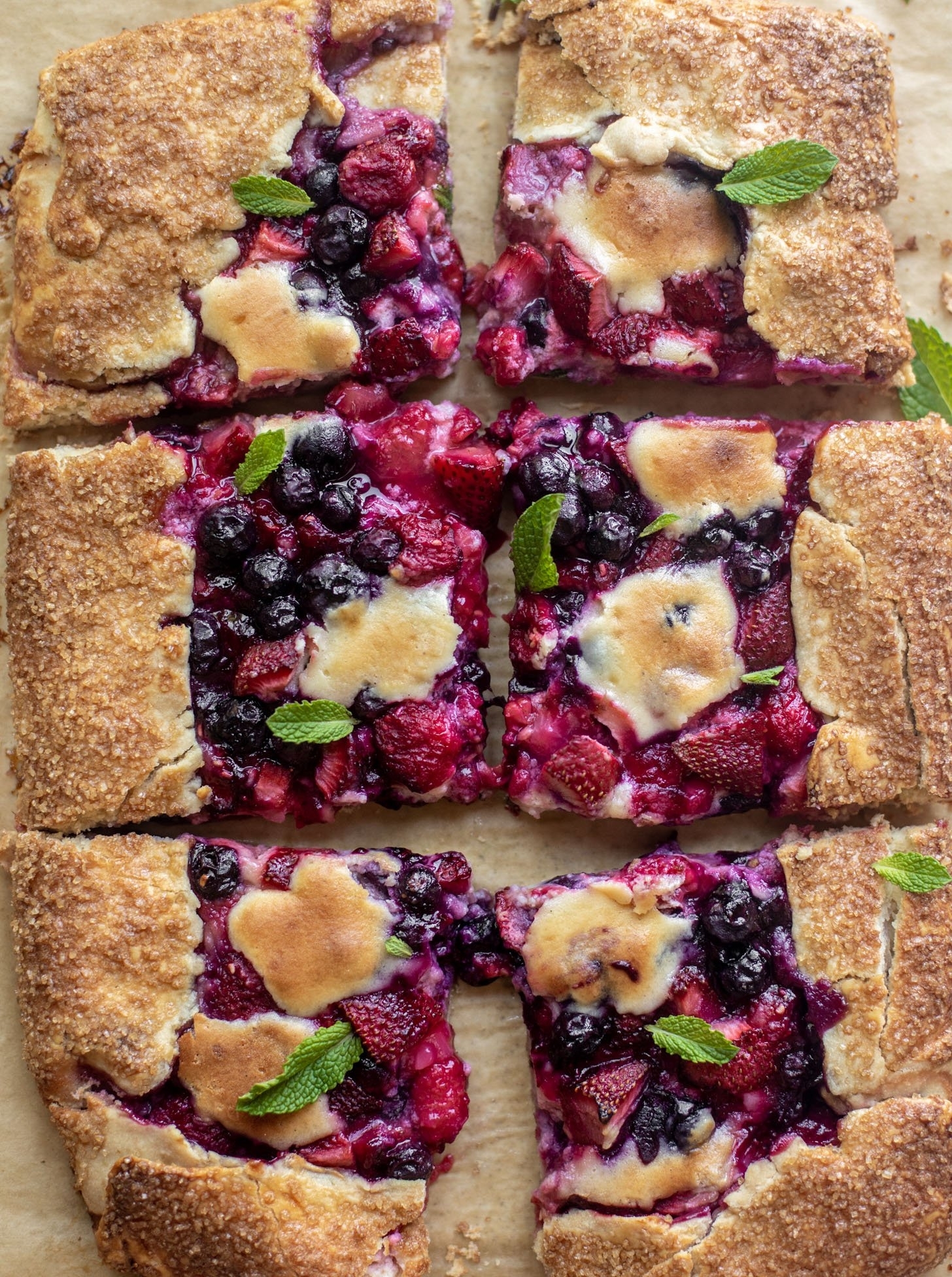 Six slices of a mixed berry galette topped with fresh mint leaves, featuring a golden-brown crust and a vibrant berry filling