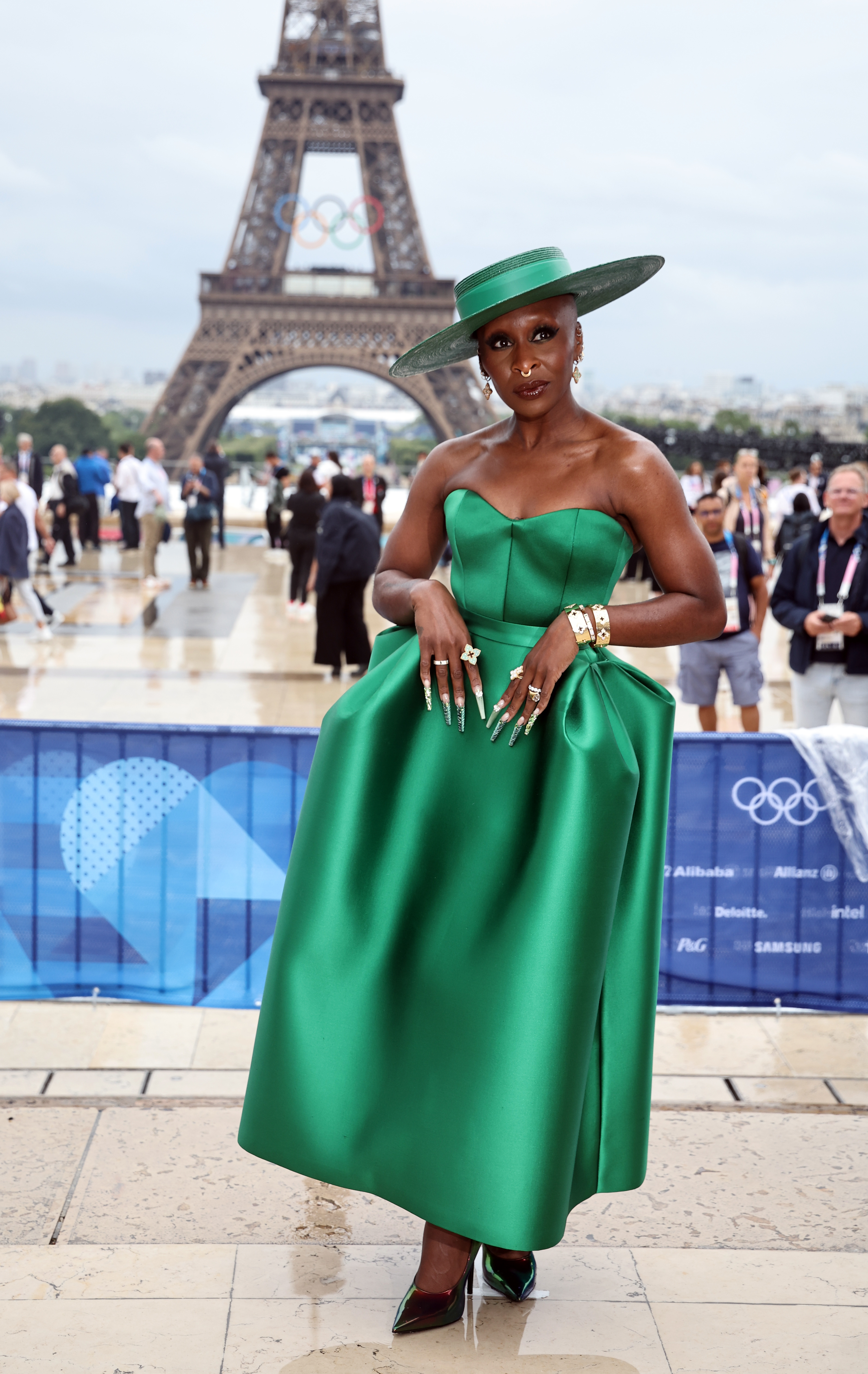 Cynthia Erivo stands in front of the Eiffel Tower wearing an elegant green dress and matching wide-brimmed hat at an event