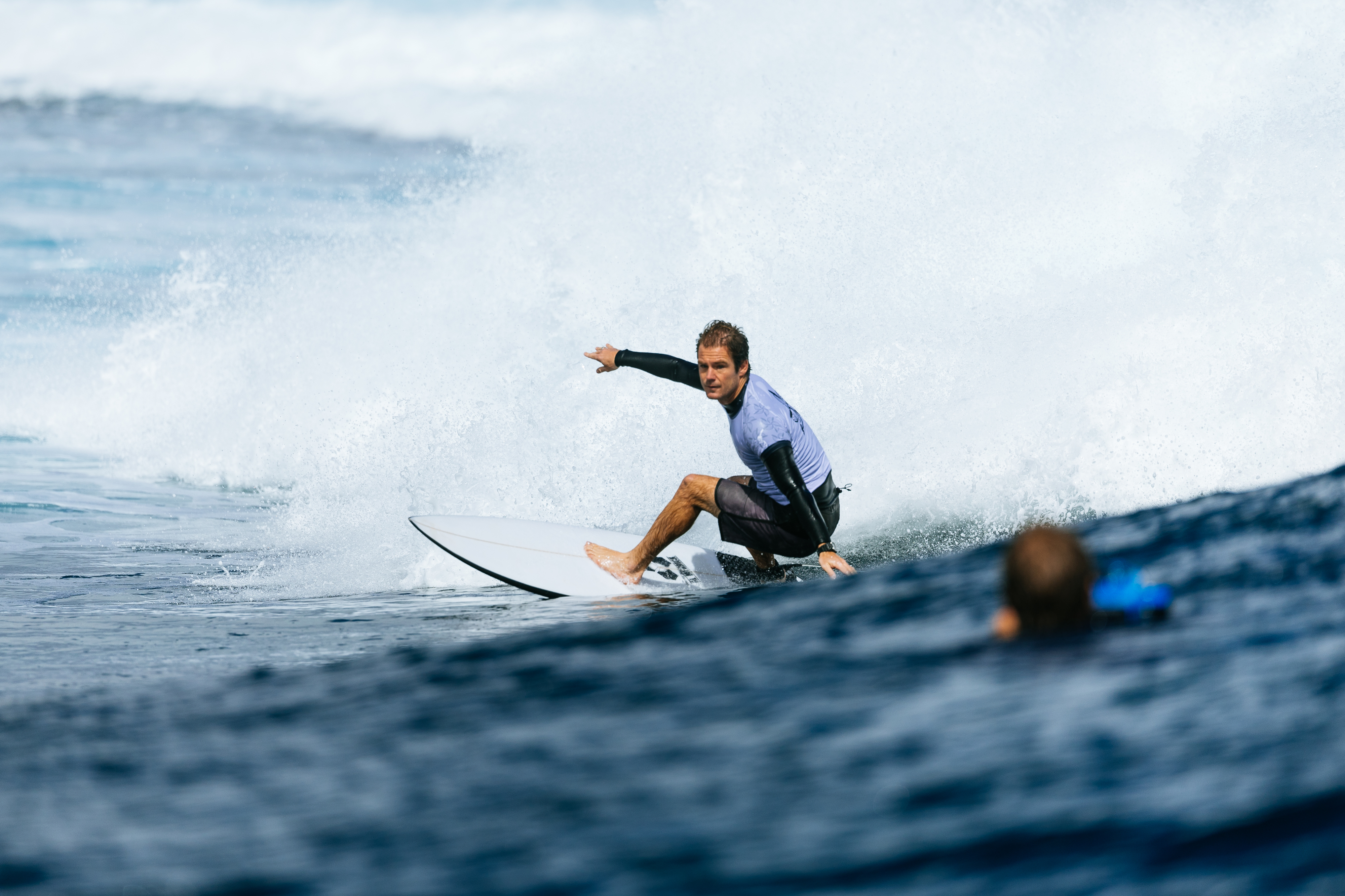 A surfer rides a wave while another person in the water watches from a distance