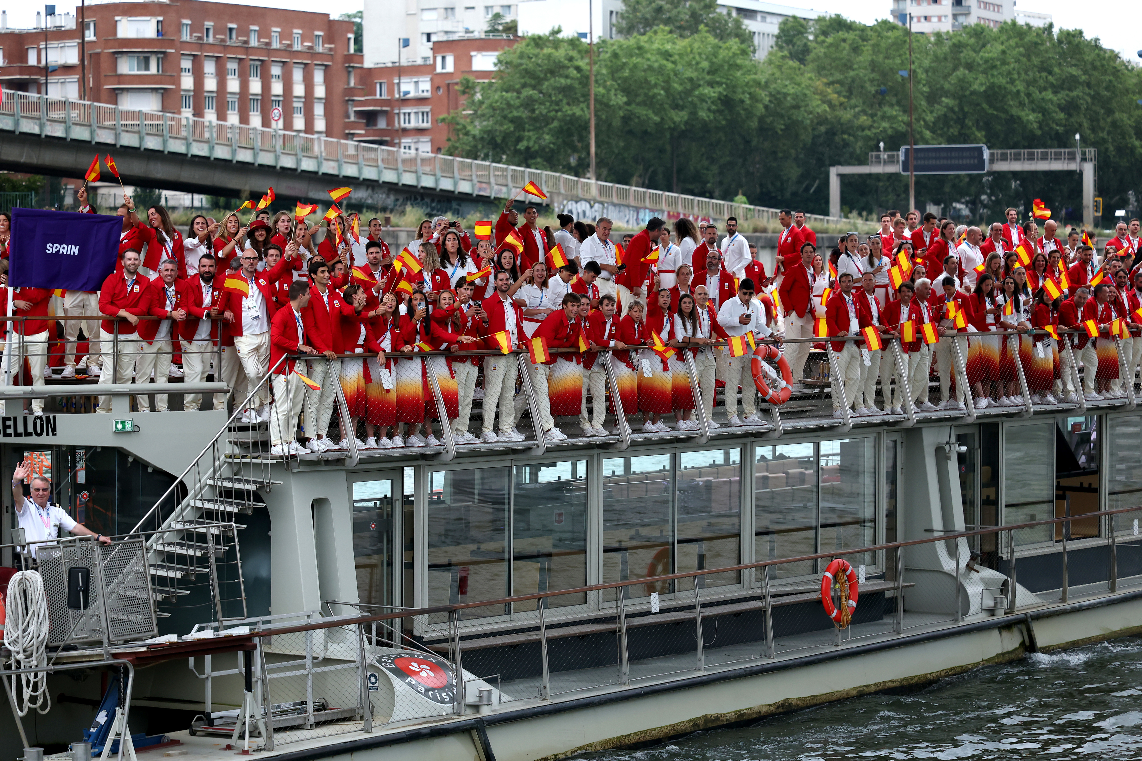 Deportistas españoles y sus equipos visten uniformes blancos y rojos con banderas de España, celebrando en un barco durante una celebración deportiva