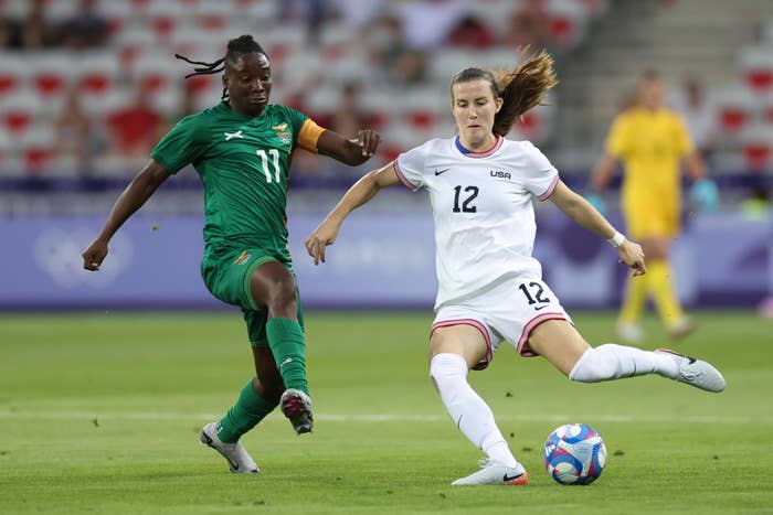 Barbara Banda and Kristie Mewis compete for the ball during a soccer match. Banda is in a green jersey, and Mewis is in a white jersey with the number 12