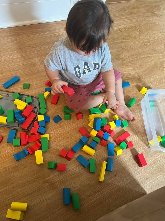 A toddler playing on the floor with colorful building blocks, wearing a gray "GAP" shirt and red shorts