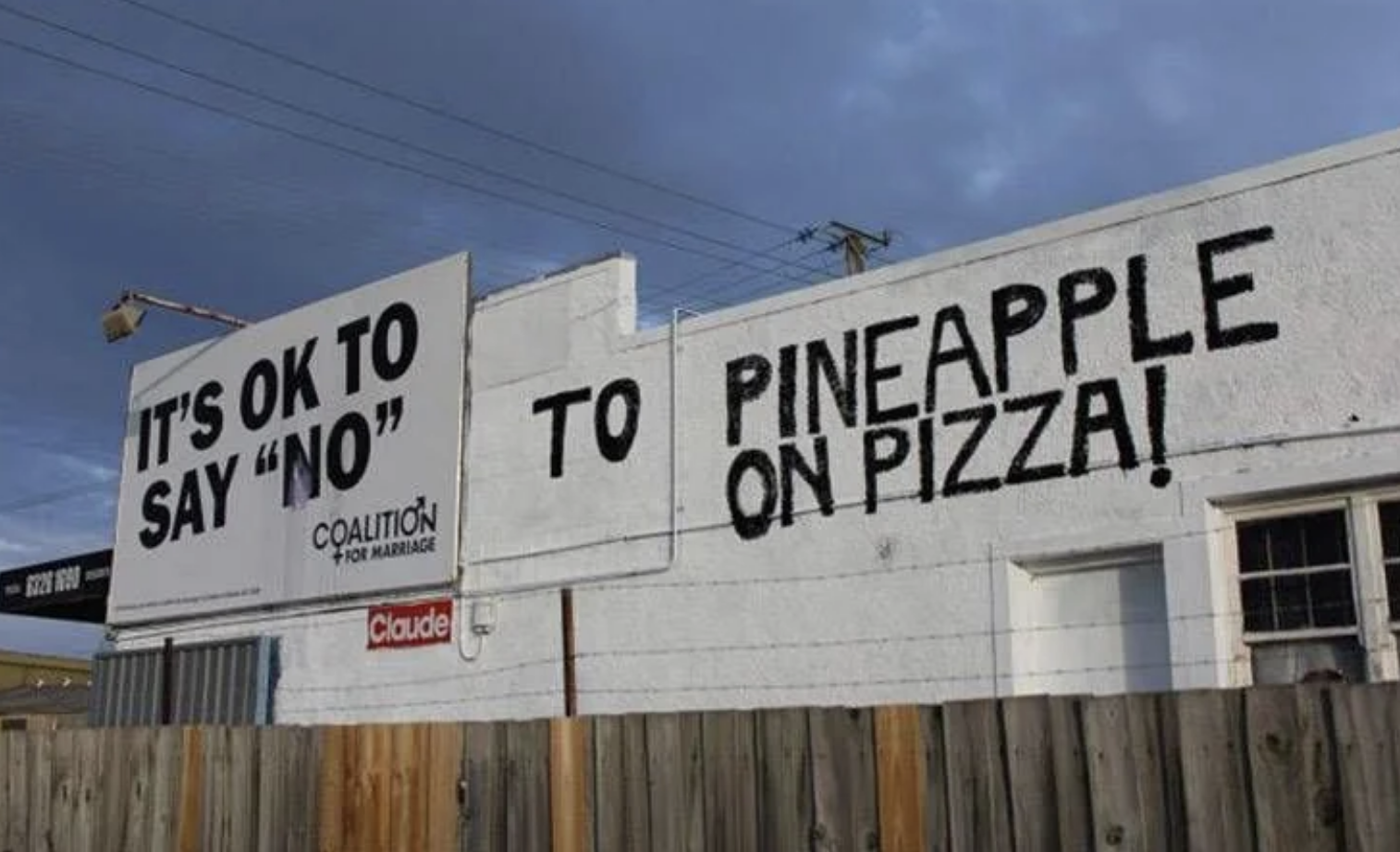 Large billboard reads, "It's OK to say 'NO' to pineapple on pizza!" with text "Coalition for Marriage Claude" and a background of an overcast sky and wooden fence