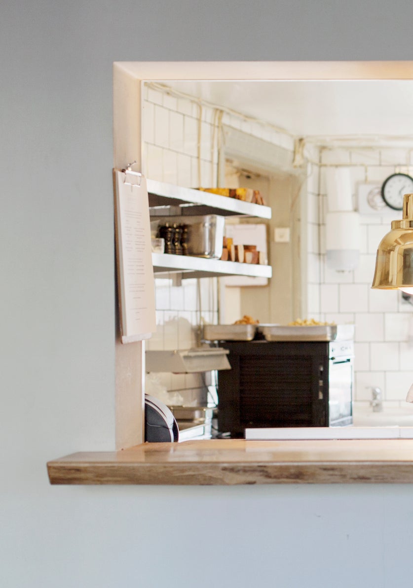 Two chefs stand in a kitchen, wearing white uniforms and aprons, discussing their work under pendant lights