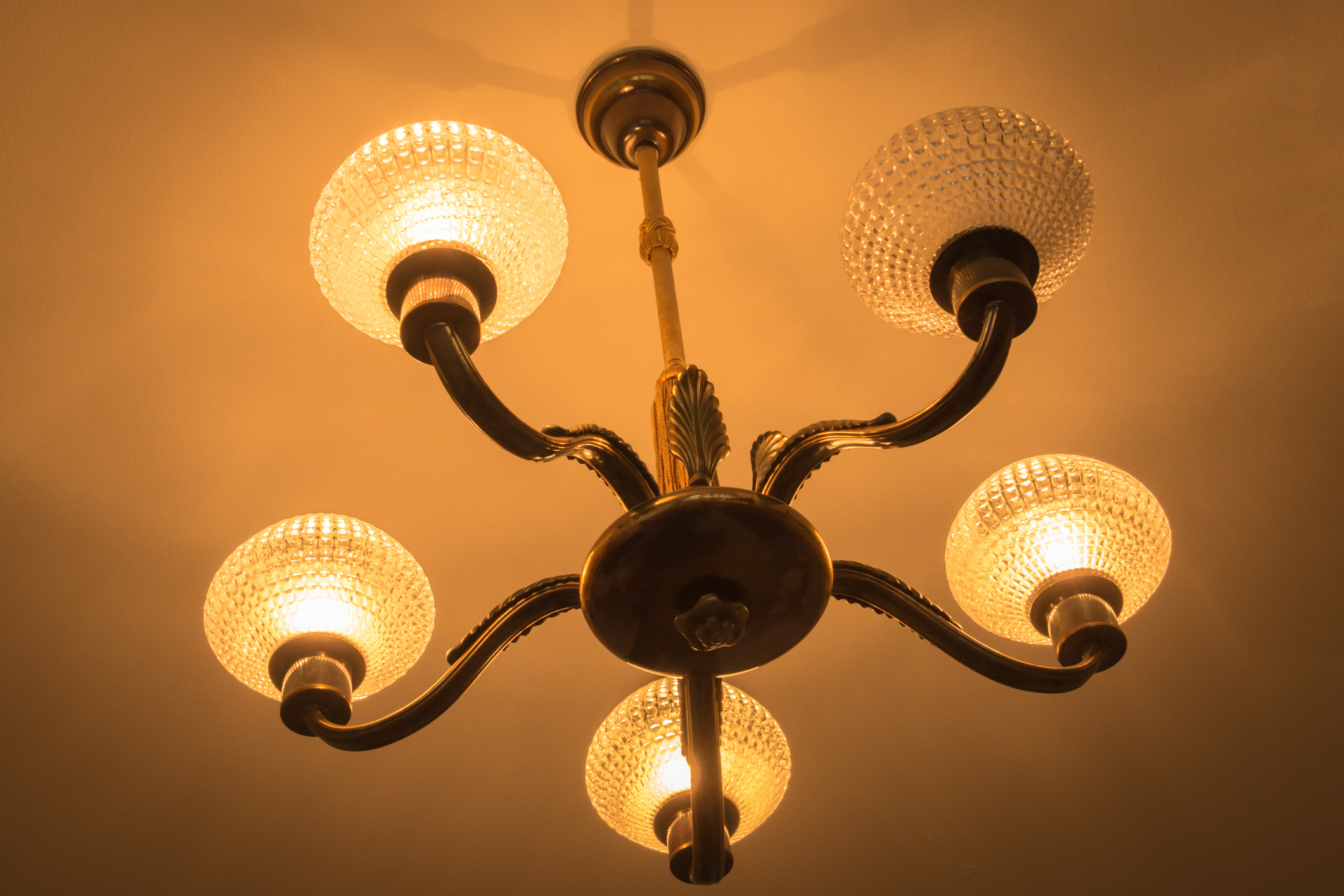 A vintage chandelier with five lit glass globes and ornate brass arms; the chandelier is mounted on a ceiling, providing warm illumination to the room