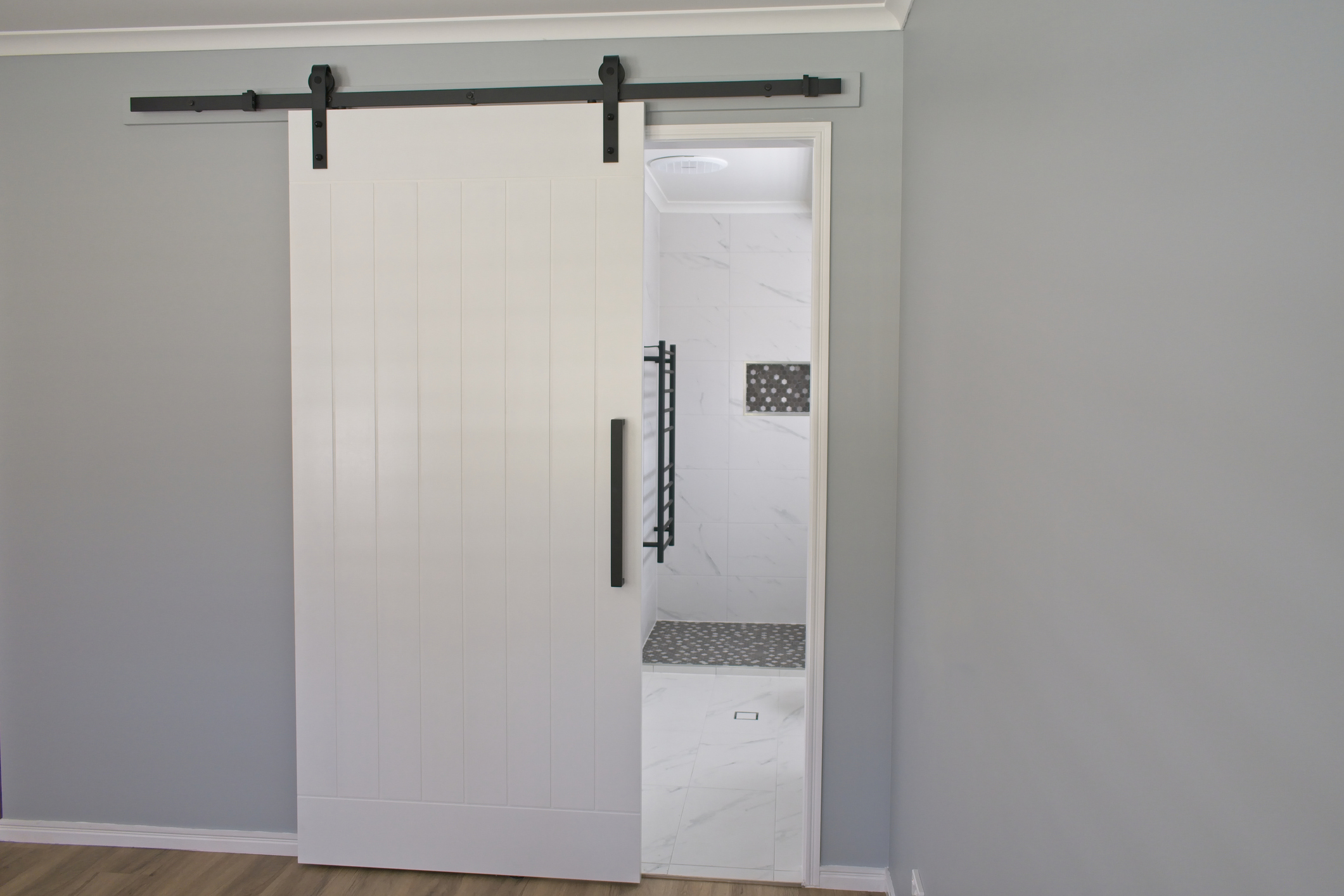 A modern interior with a white sliding barn door partially open, revealing a clean, minimalistic bathroom