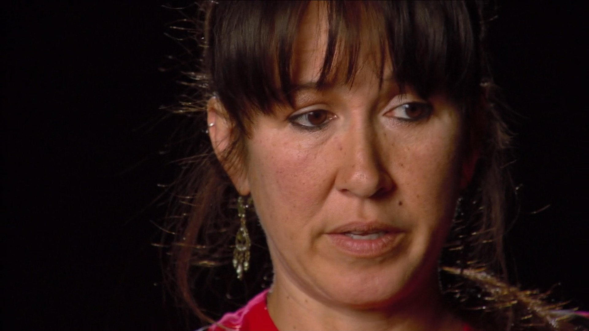 Mary Vincent, with earrings and bangs is looking to the side with a serious expression. Her hair is tied back.
