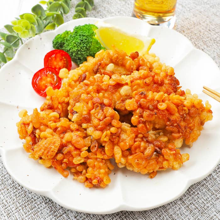 白い皿に盛り付けられた揚げ料理。レモンのくし切り、ブロッコリー、プチトマトが添えられている。背景に緑の植物が見える。