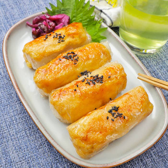 皿に盛られた焼いた料理が4つ、上にはゴマがのっている。隣に箸と緑色の飲み物があります。