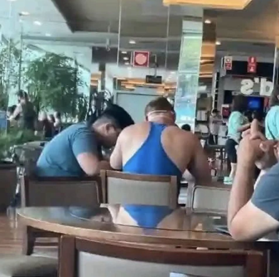 Two people seated with their backs facing the camera, leaning towards each other at a restaurant table indoors