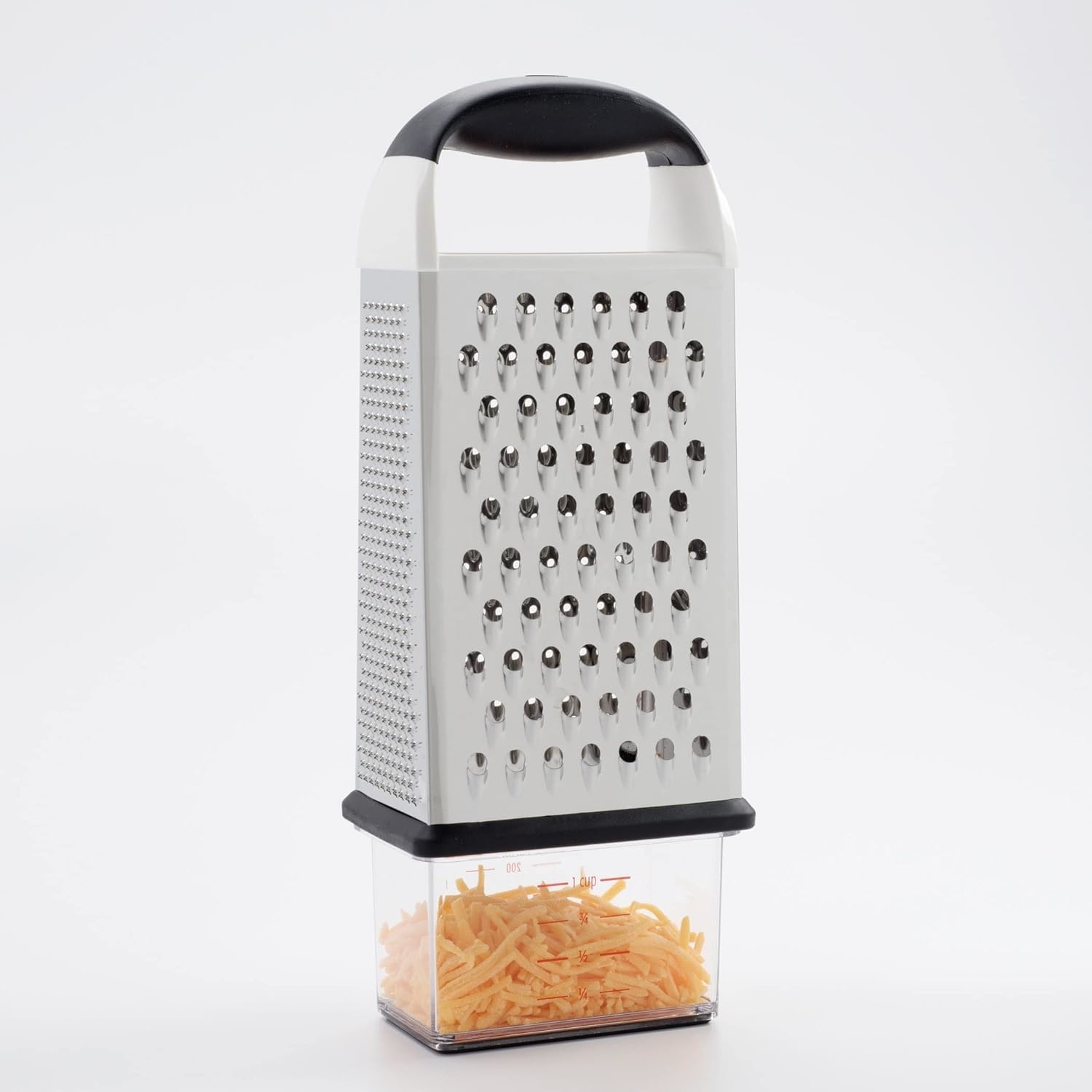 A metal box grater with a black handle is placed over a clear container filled with shredded cheese