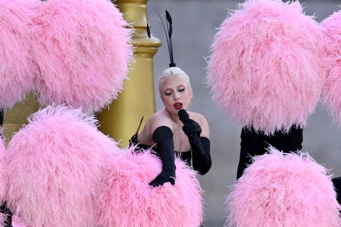 Lady Gaga performs amid large pink feathered fans while wearing black gloves and a black outfit