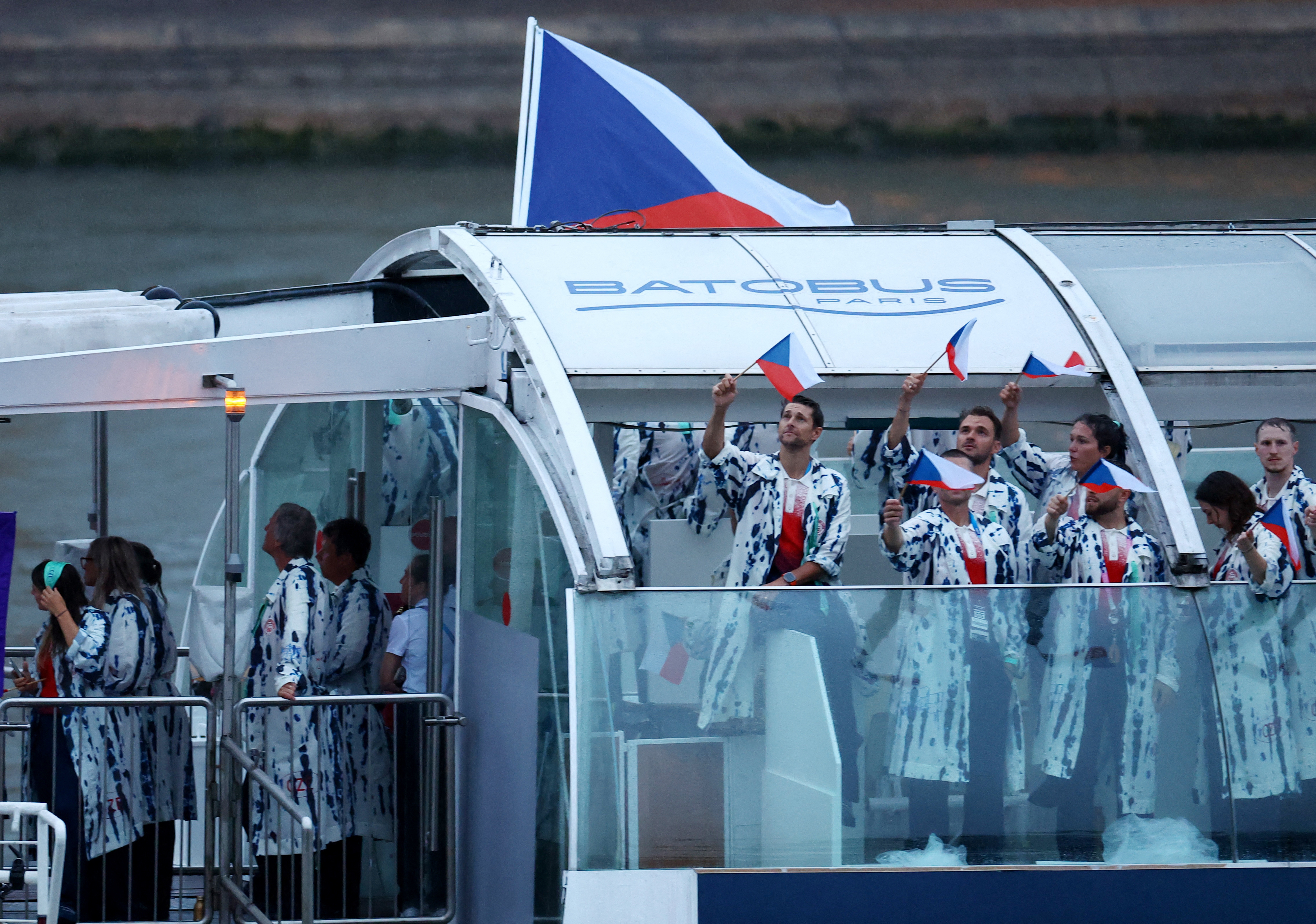 Group of people in matching patterned jackets wave small flags on a boat under a "Batobus Paris" sign