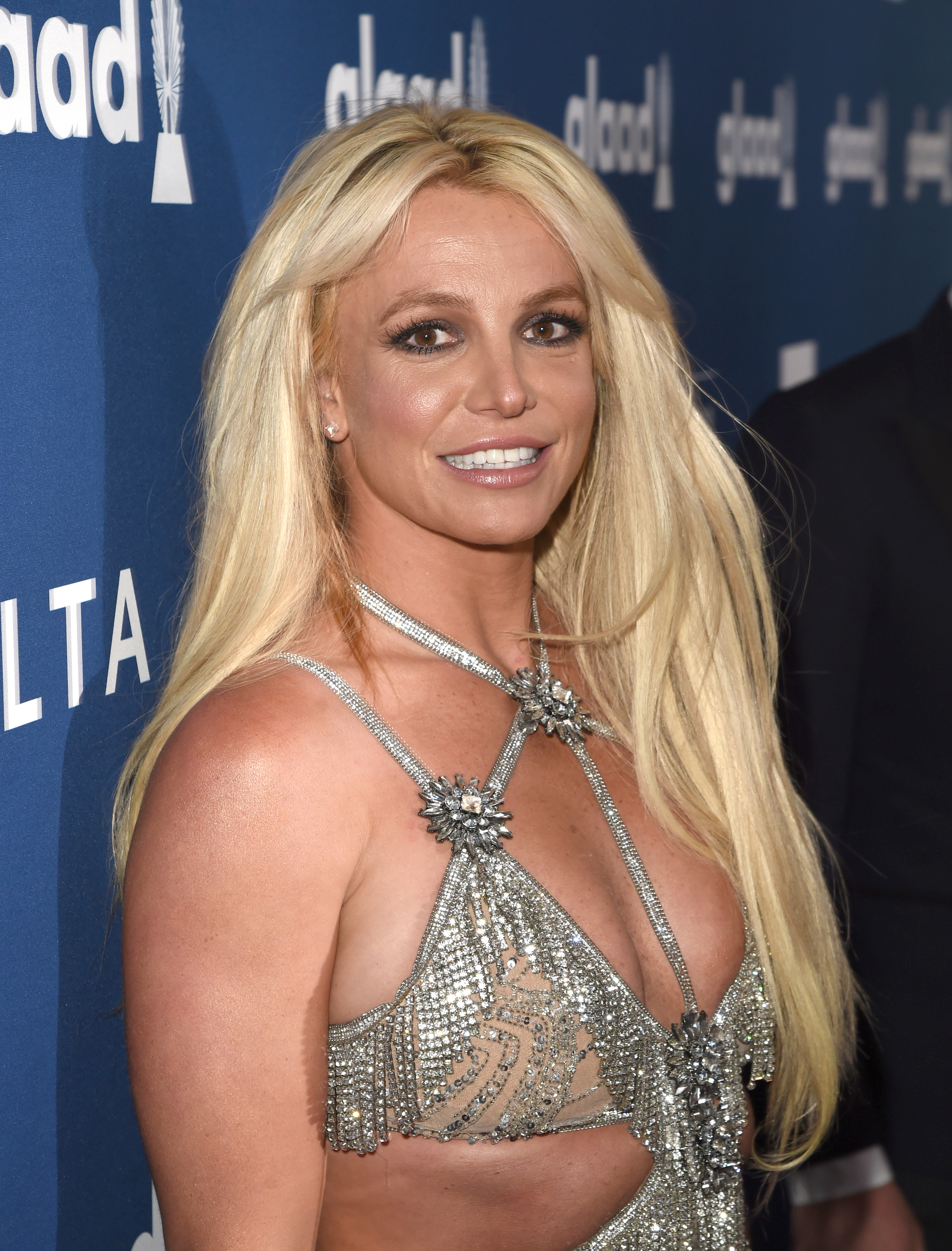 Britney Spears at the GLAAD Media Awards, wearing a sparkly, detailed silver dress with cut-outs and long blonde hair