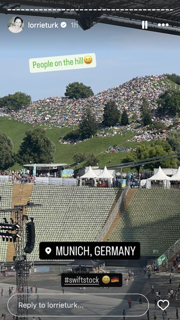 A large crowd sits on a grassy hill overlooking an event in a stadium in Munich, Germany. Text reads "People on the hill" and "#swiftstock."