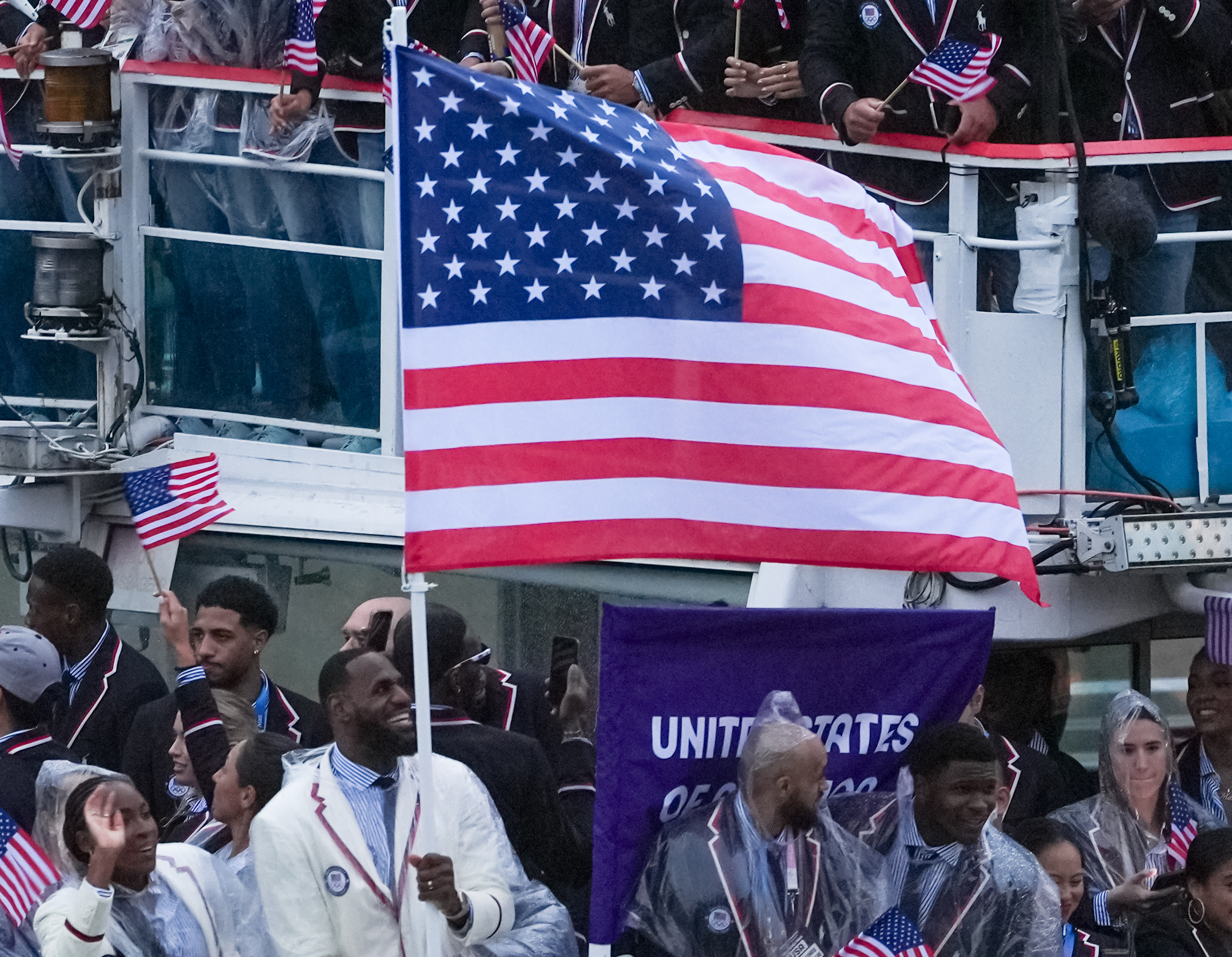 People waving American flags, many in matching outfits with white jackets and black pants, are celebrating, including one person holding a large U.S. flag