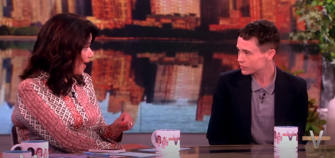 Sheryl Underwood and Elliot Page in a discussion on the set of "The View" talk show. Both are seated with mugs on the table