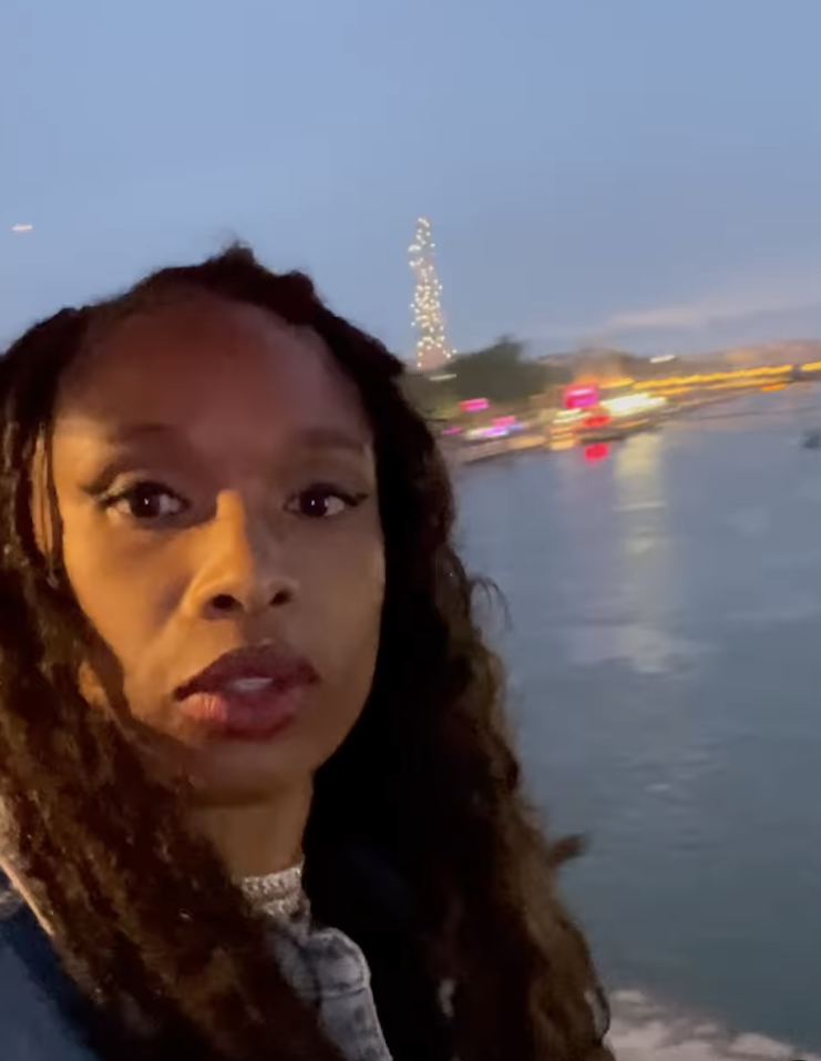 Jennifer Hudson takes a selfie near a waterfront with city lights in the background