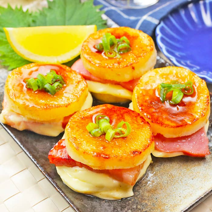 ベーコンを挟んだチーズ付きの料理。ネギがトッピングされています。背景にはレモンと青い皿があります。