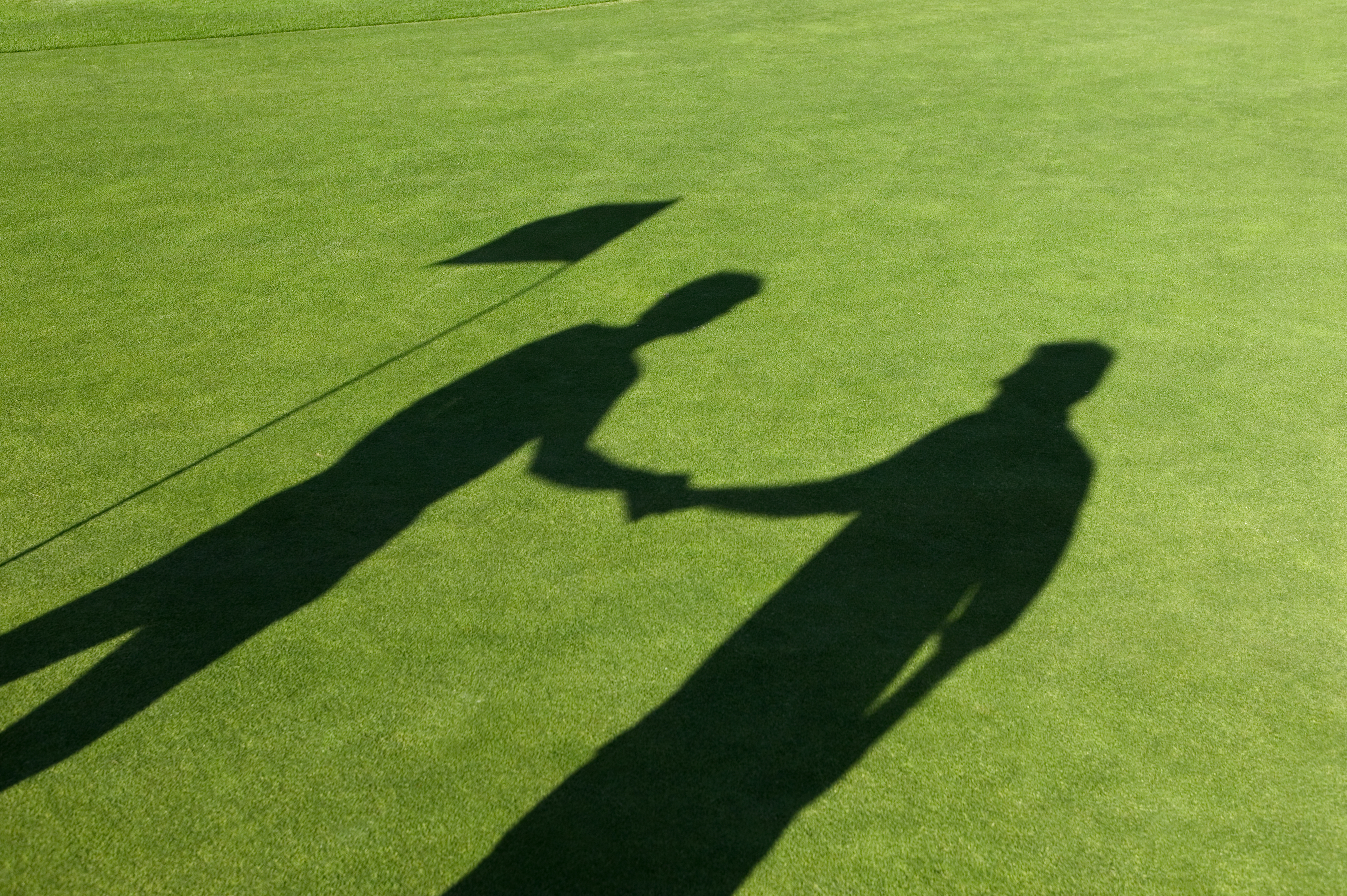 Silhouettes of two people shaking hands on a golf course next to a flag