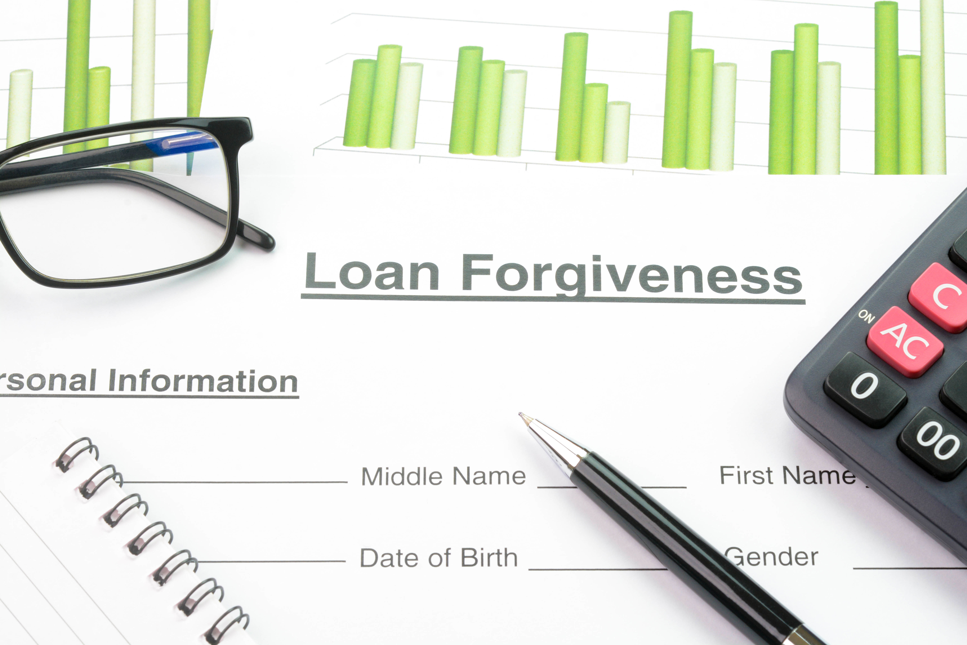 Glasses, a pen, a calculator, and documents with text &quot;Loan Forgiveness&quot; and personal information fields. Charts with vertical bars are in the background
