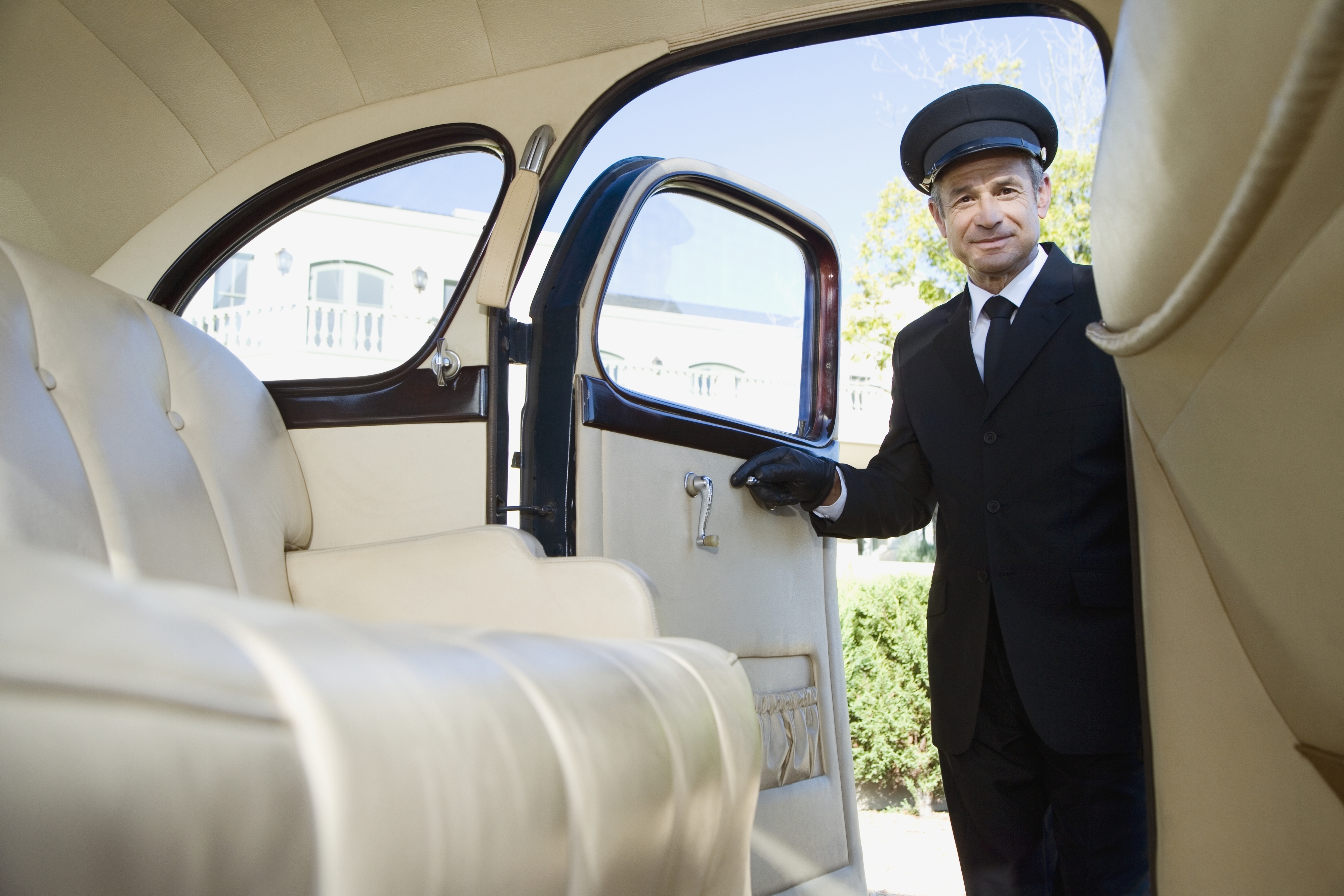 Chauffeur in uniform opens a car door, ready to assist passengers, showcasing a high level of service and professionalism