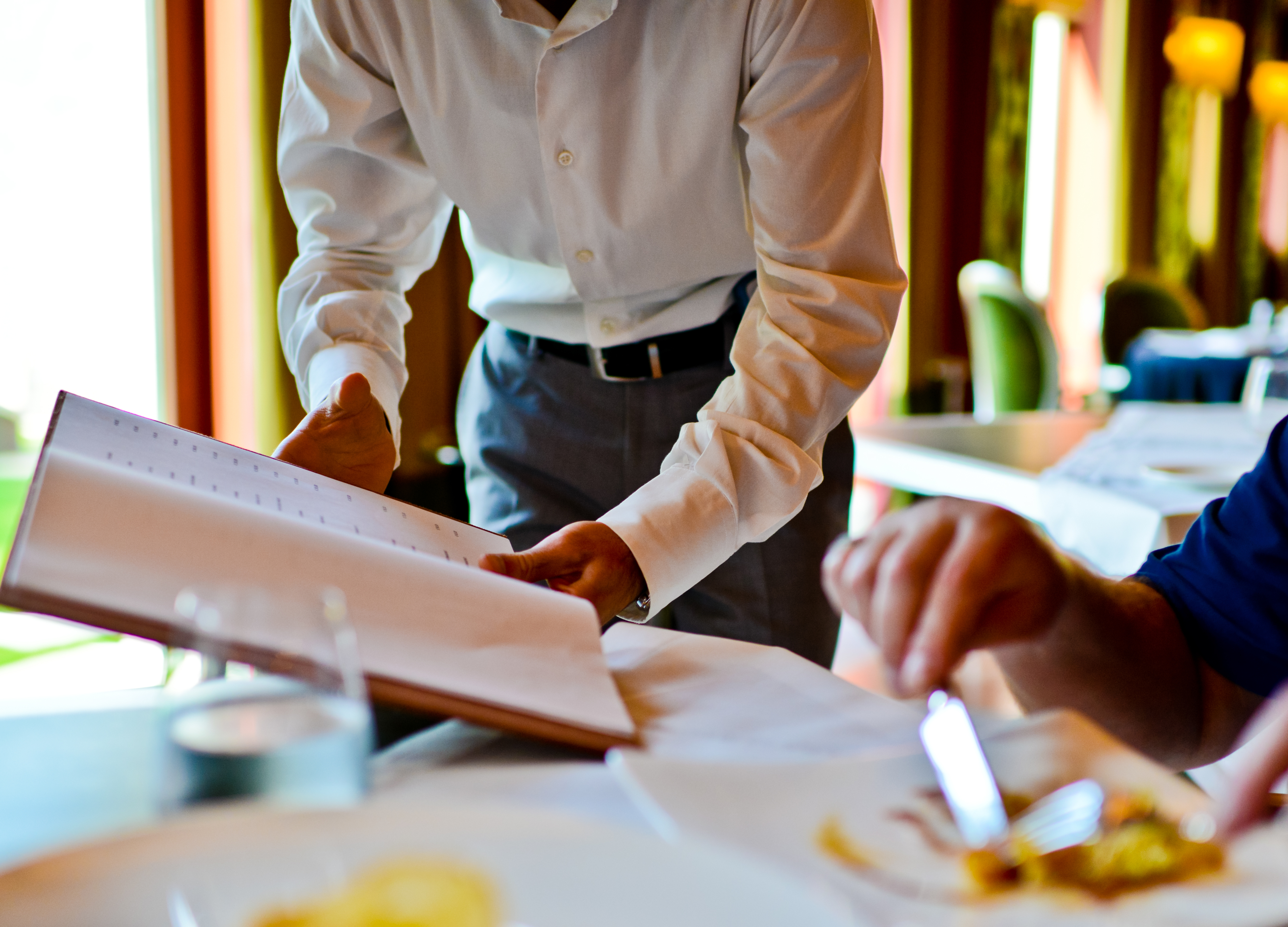 A waiter showing a menu to a seated customer in a restaurant setting