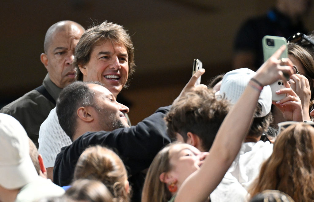 Tom Cruise smiles while people around him take selfies and photos