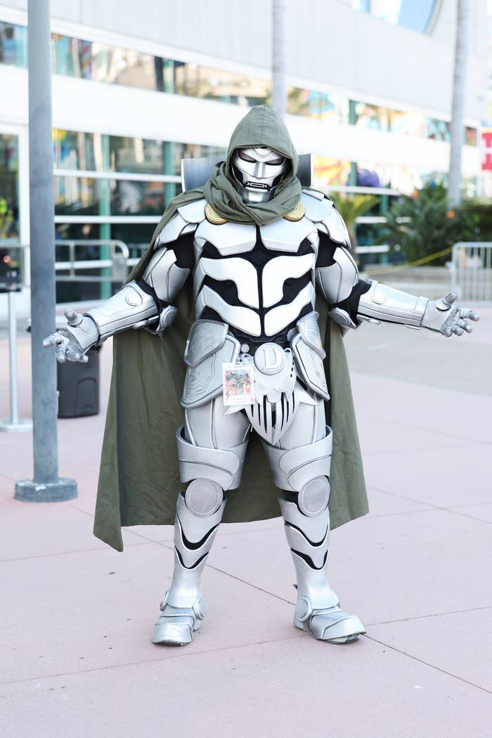 Person in a detailed Dr. Doom cosplay costume stands with arms slightly outstretched at an outdoor event area