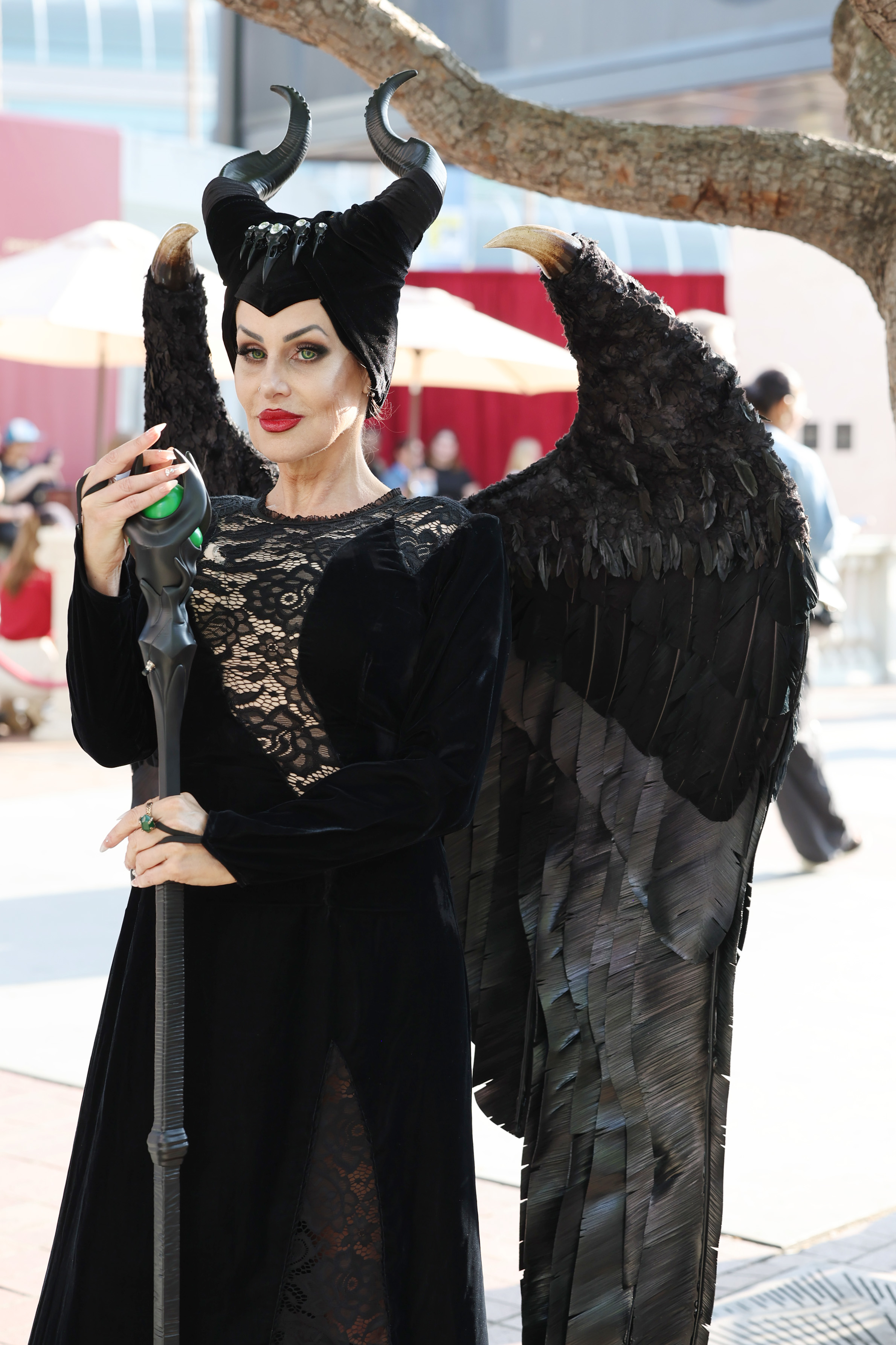 Person dressed as Maleficent, in a black gown with lace, black headdress with horns, and large black wings, holding a staff with a green orb